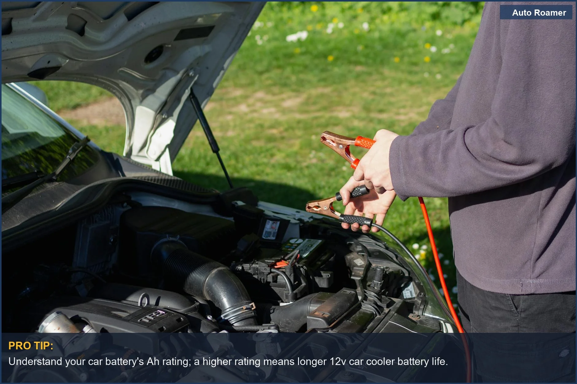 Man using jumper cables on car engine outdoors, illustrating car fridge battery drain concerns on a sunny day.