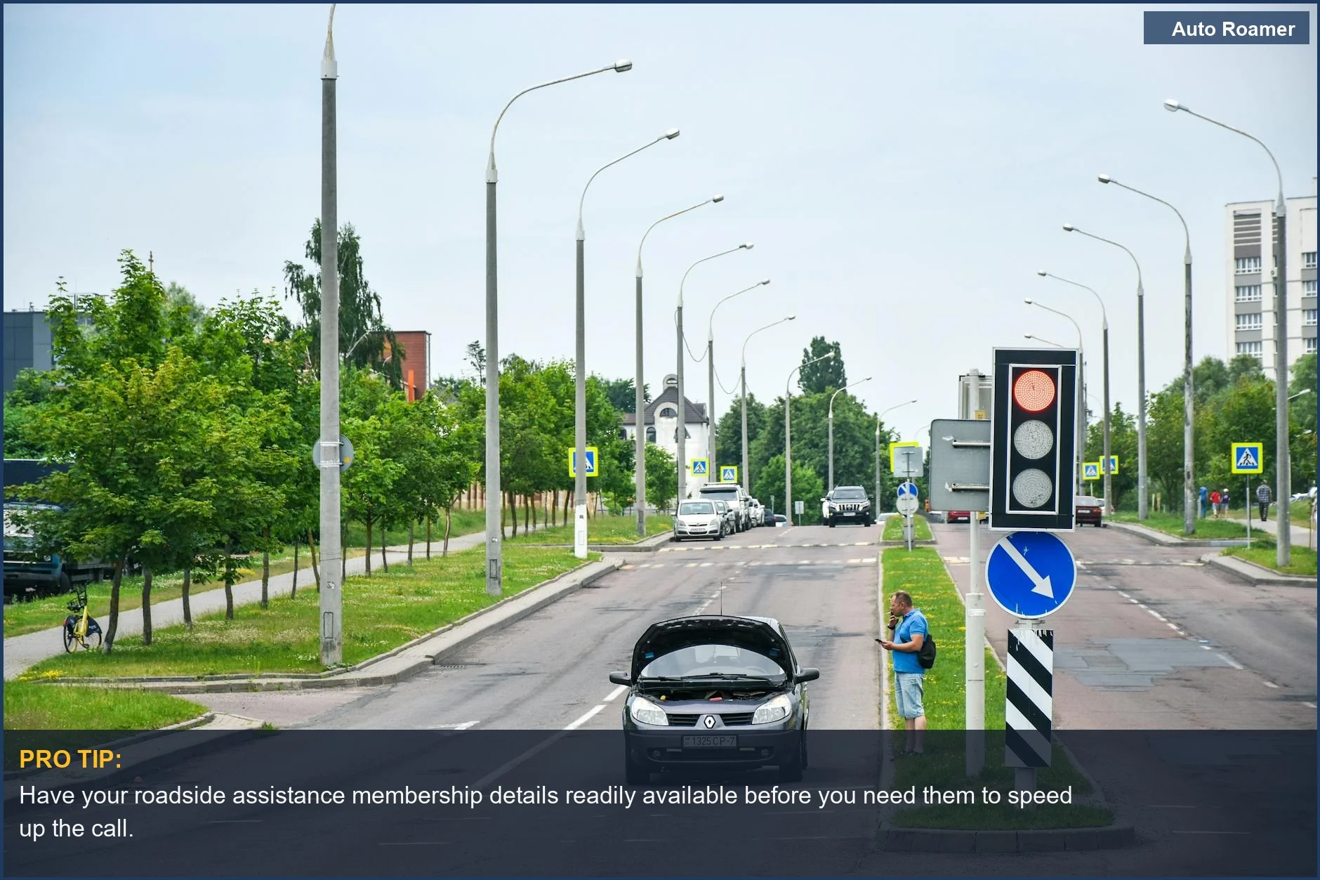 Man on city street checks his phone while standing beside a car needing roadside assistance.