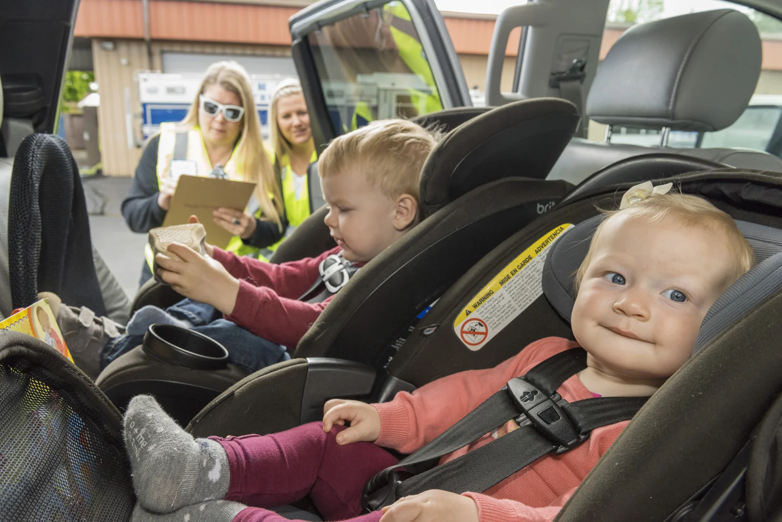 Young children buckled into child car seats in the back of a vehicle, illustrating the family road-trip context for planning rest stops.