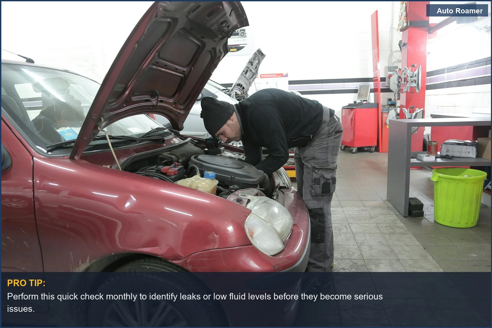 Mechanic inspecting red car engine for essential car fluids check in a garage workshop.