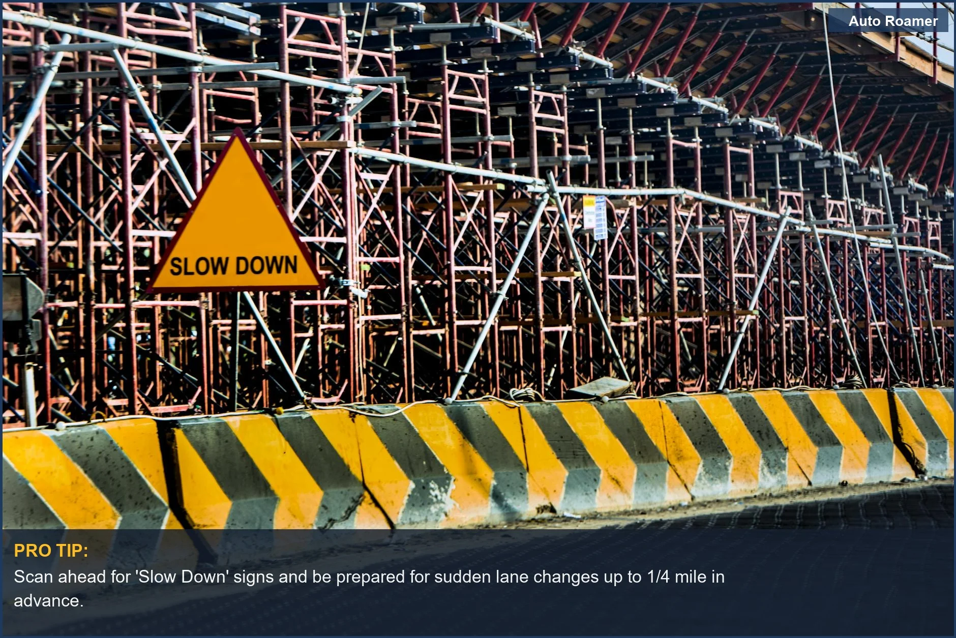 Road construction site with a 'Slow Down' sign and scaffolding, emphasizing construction zone driving safety.