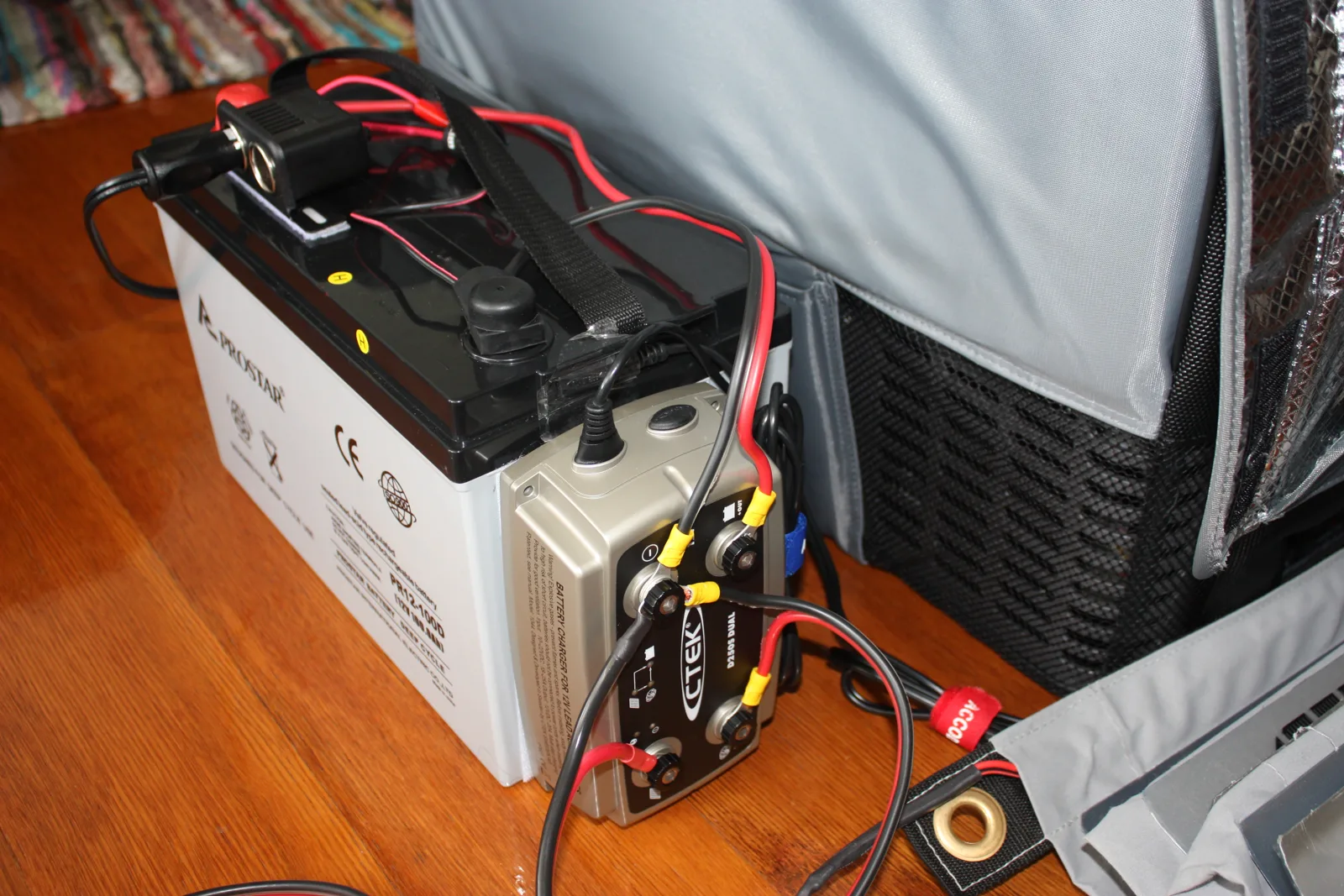 A deep-cycle auxiliary battery wired to a charger beside a 12V fridge, the separate-battery fix this car-battery guide recommends