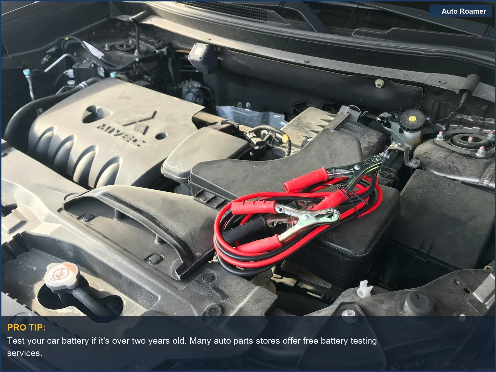 Red jumper cables connected to a car engine, illustrating battery maintenance for summer.