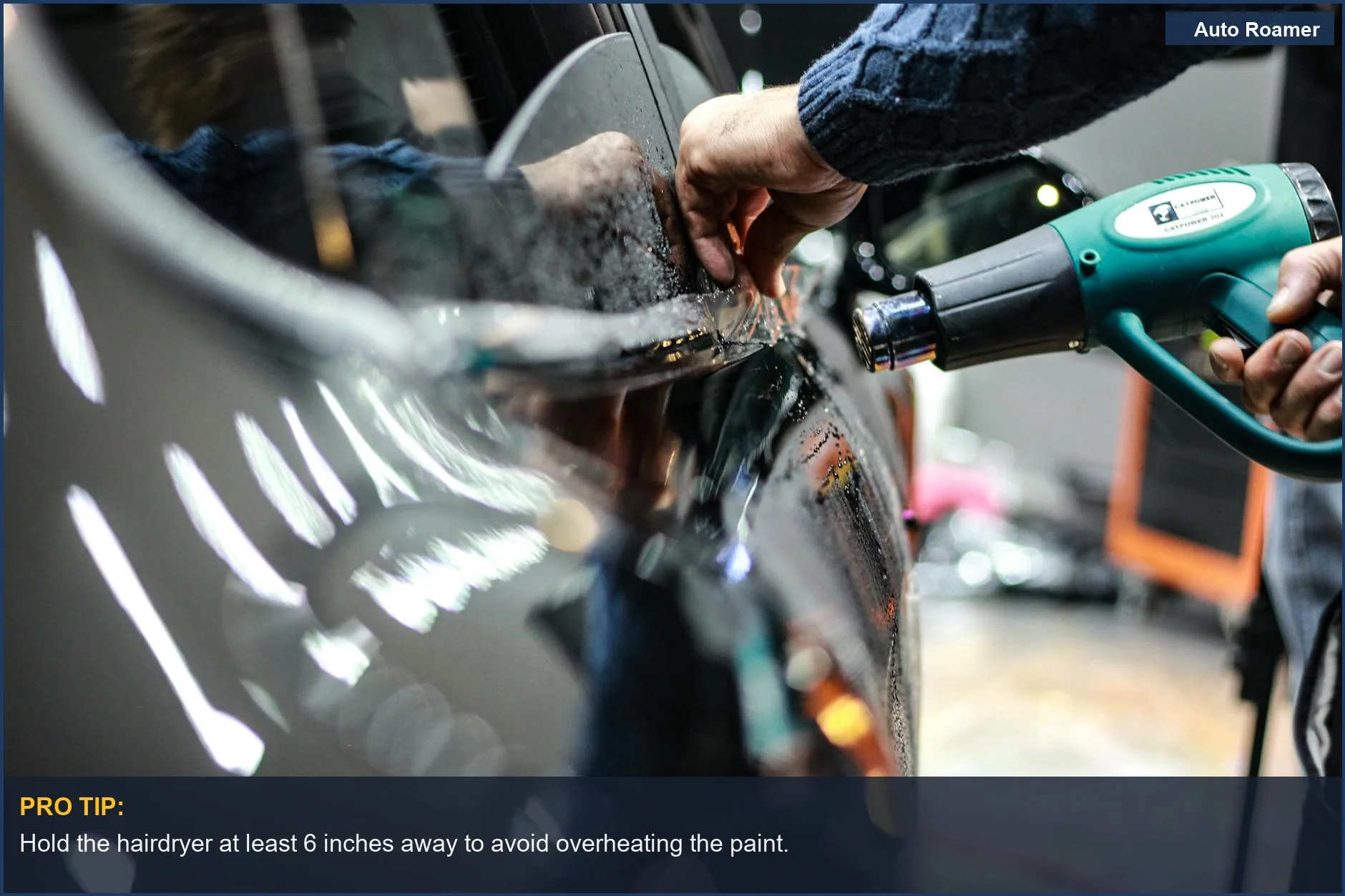 Close-up of a heat gun used for precise bumper sticker removal in a garage.