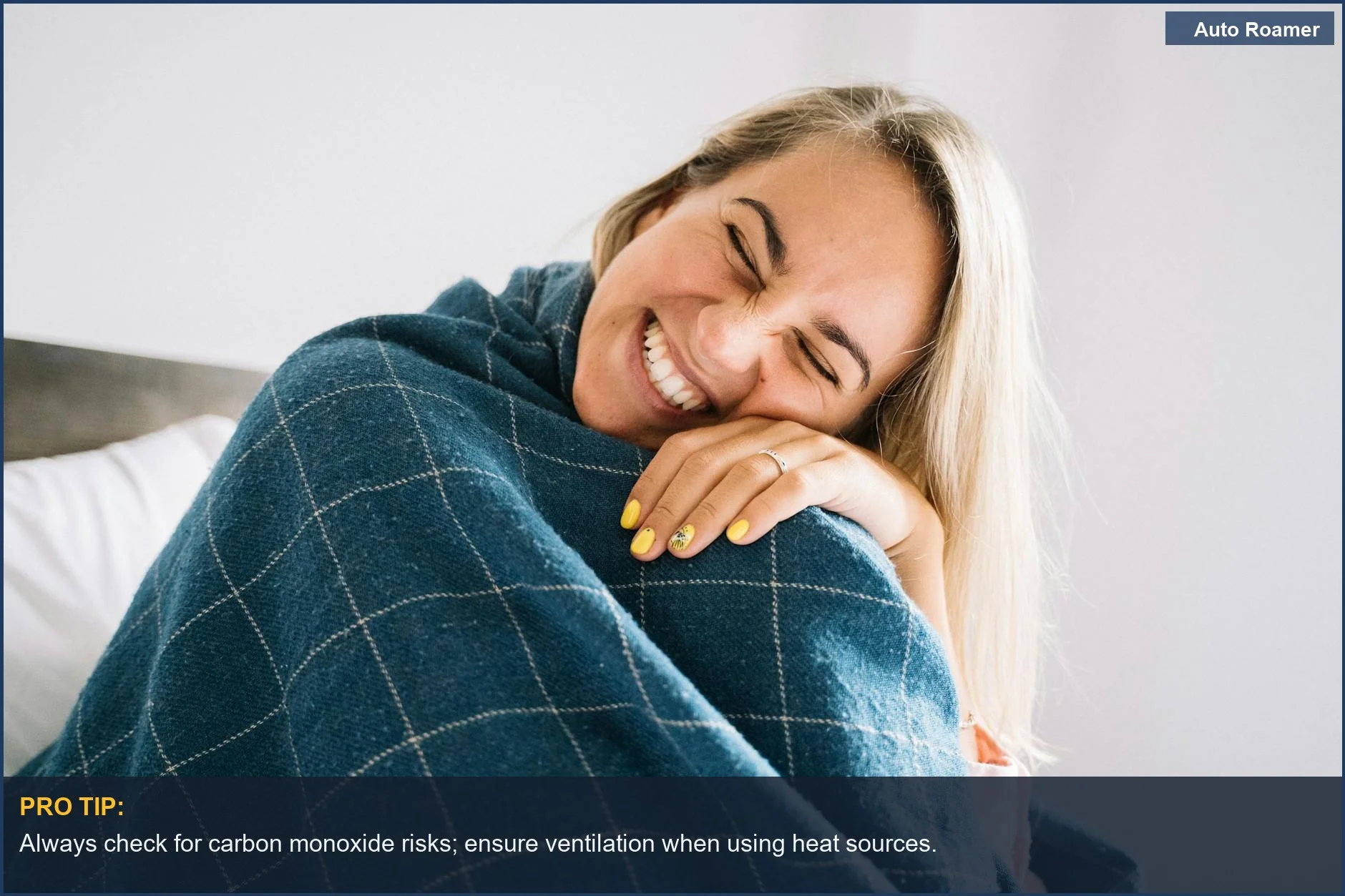 Happy woman wrapped in a blue blanket indoors, radiating warmth and comfort.