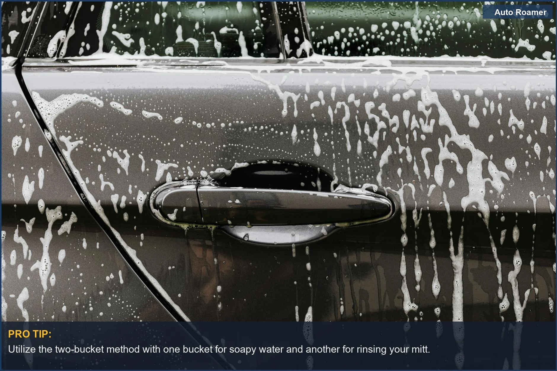 Detailed view of soap suds on black car door, illustrating the two bucket car wash method.