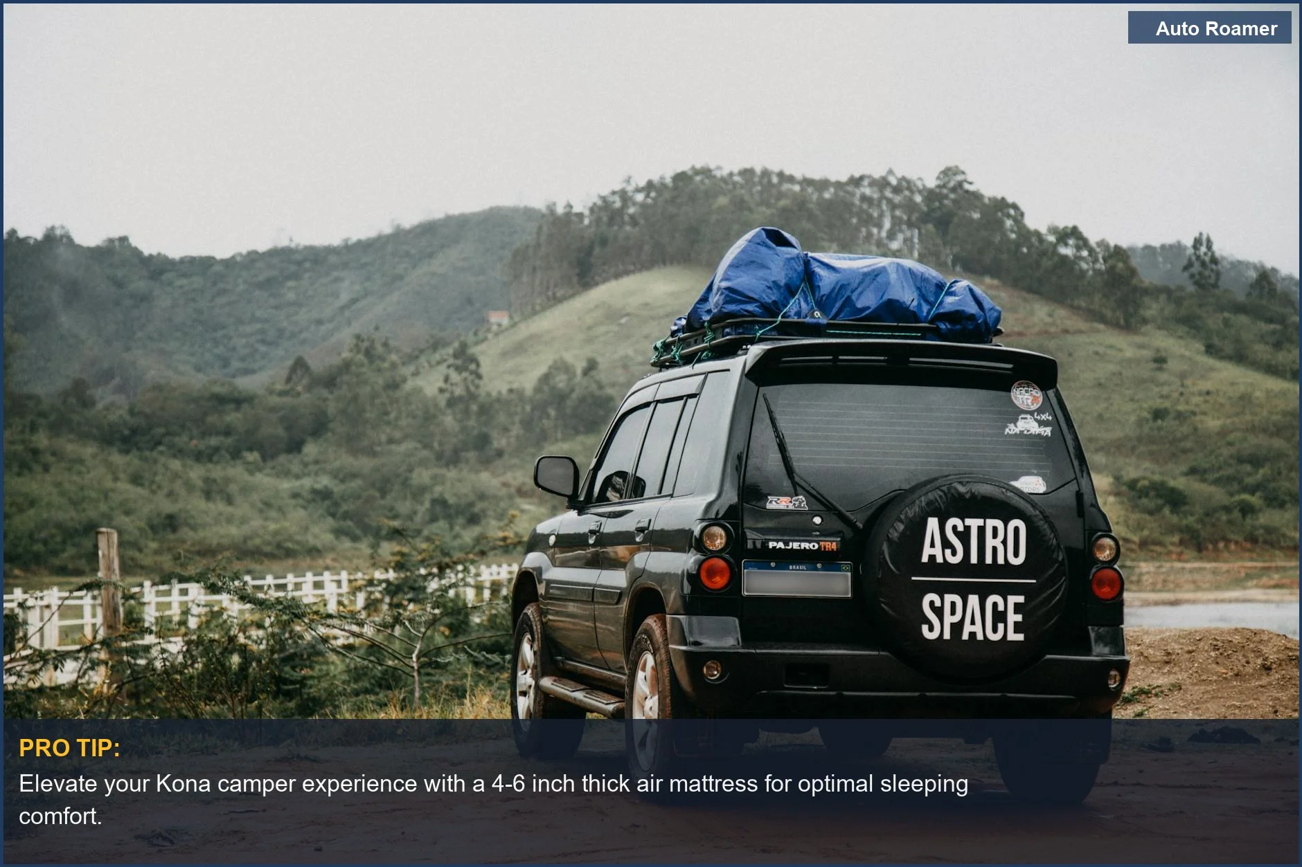 Black Hyundai Kona with roof rack parked near lush green hills and dirt path.