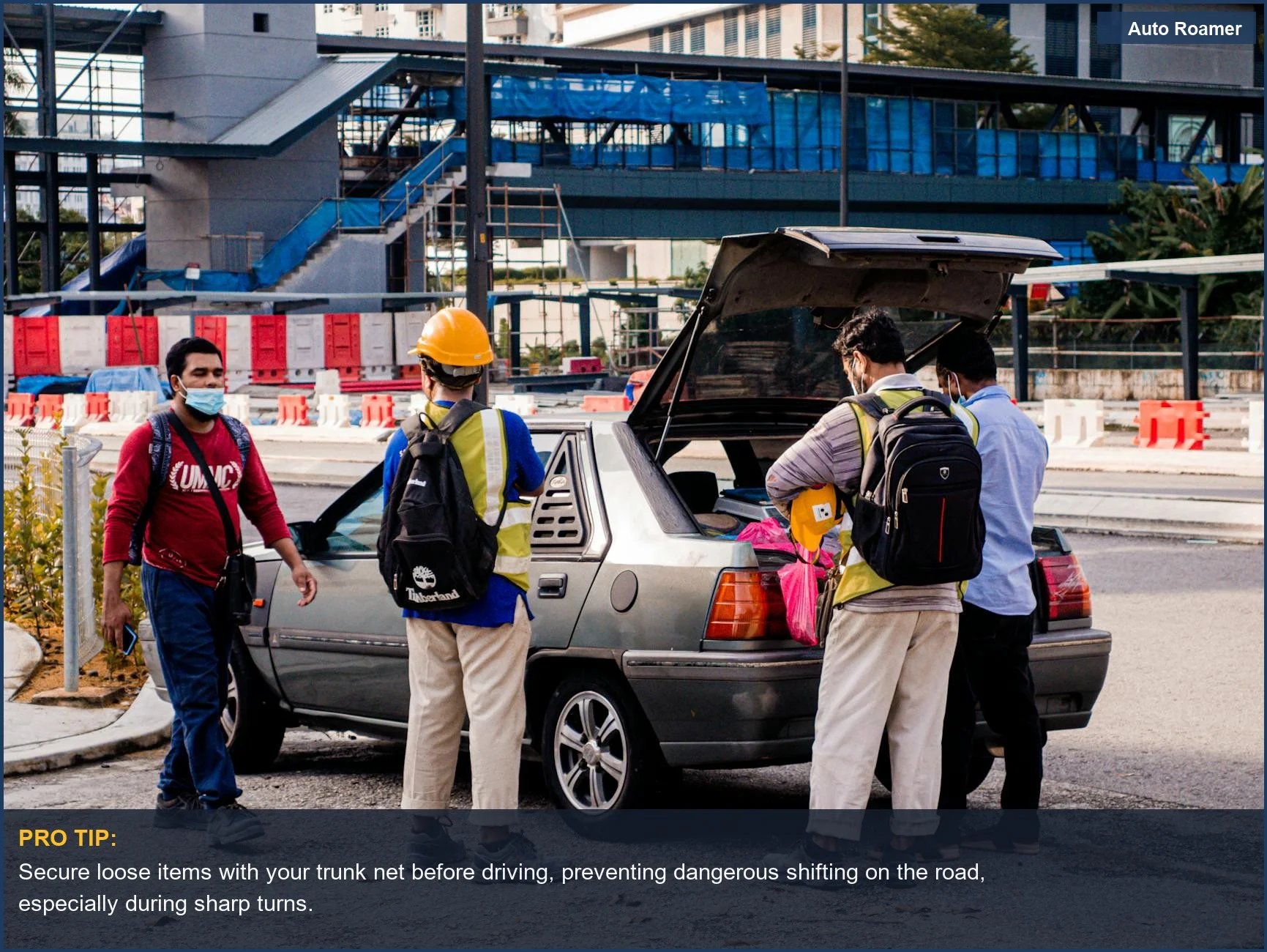 Workers in safety gear securing items in a car trunk near a construction site.