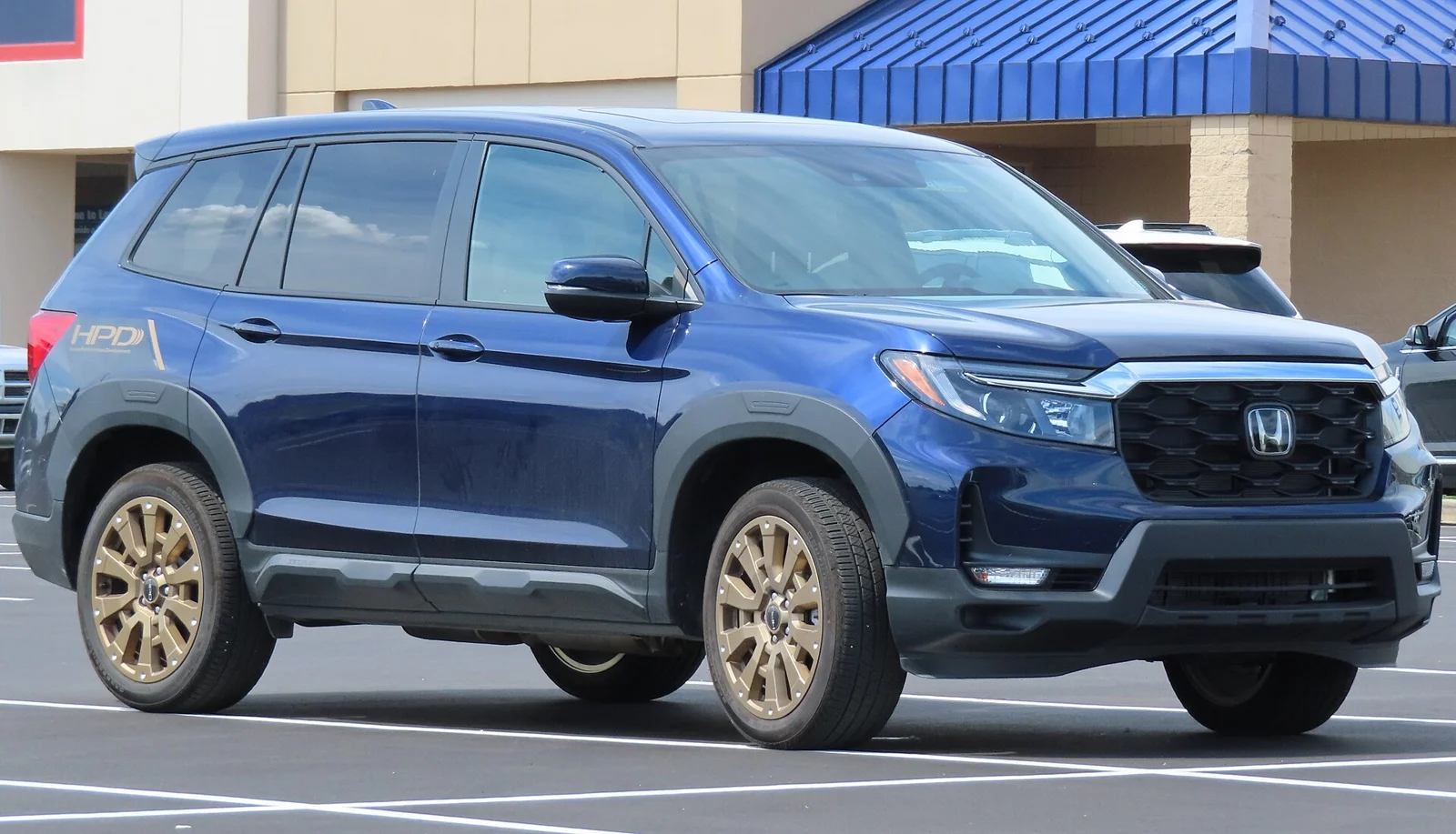 Blue Honda Passport TrailSport, current third generation, front three-quarter view with bronze-finish alloy wheels in a parking lot.