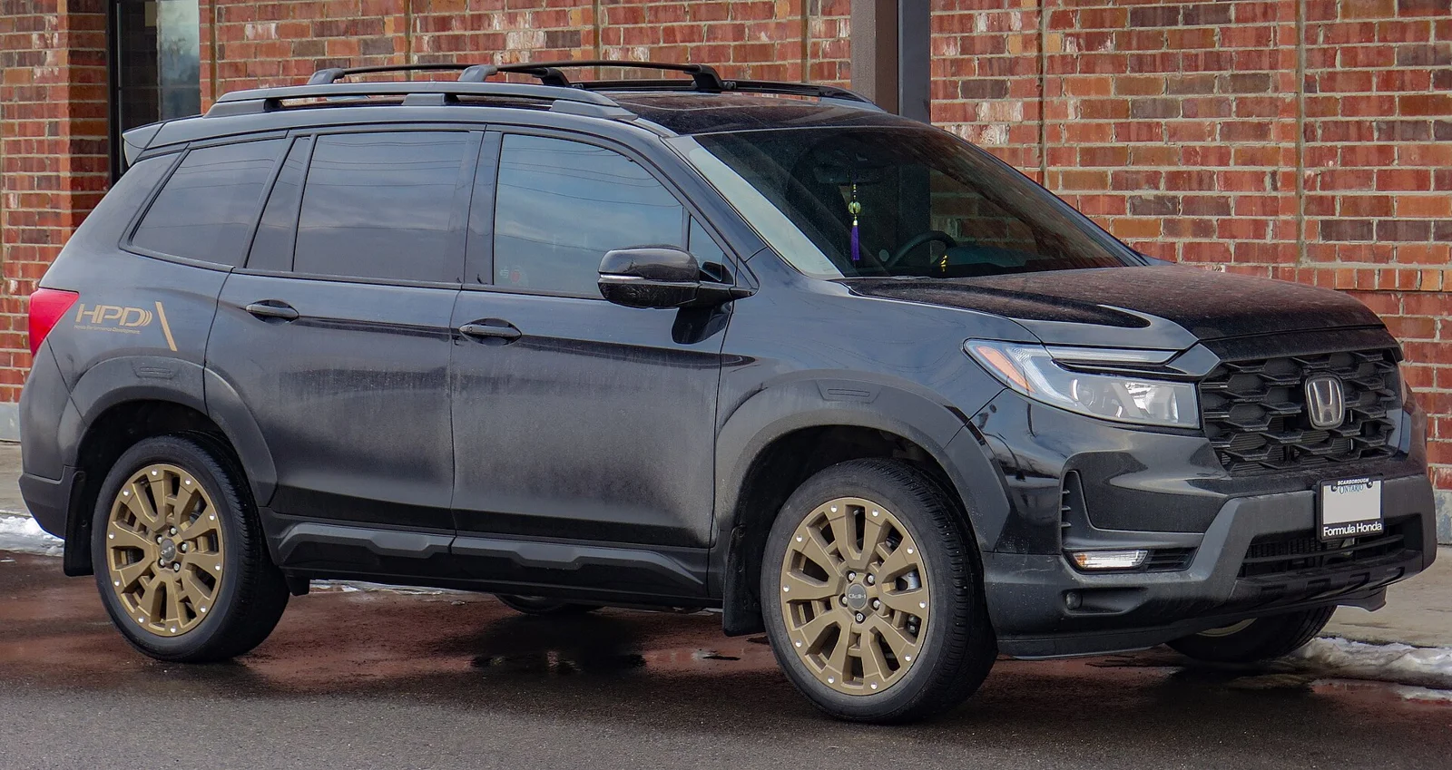 Dark-gray Honda Passport TrailSport, current third generation, front three-quarter view with bronze wheels against a brick wall.