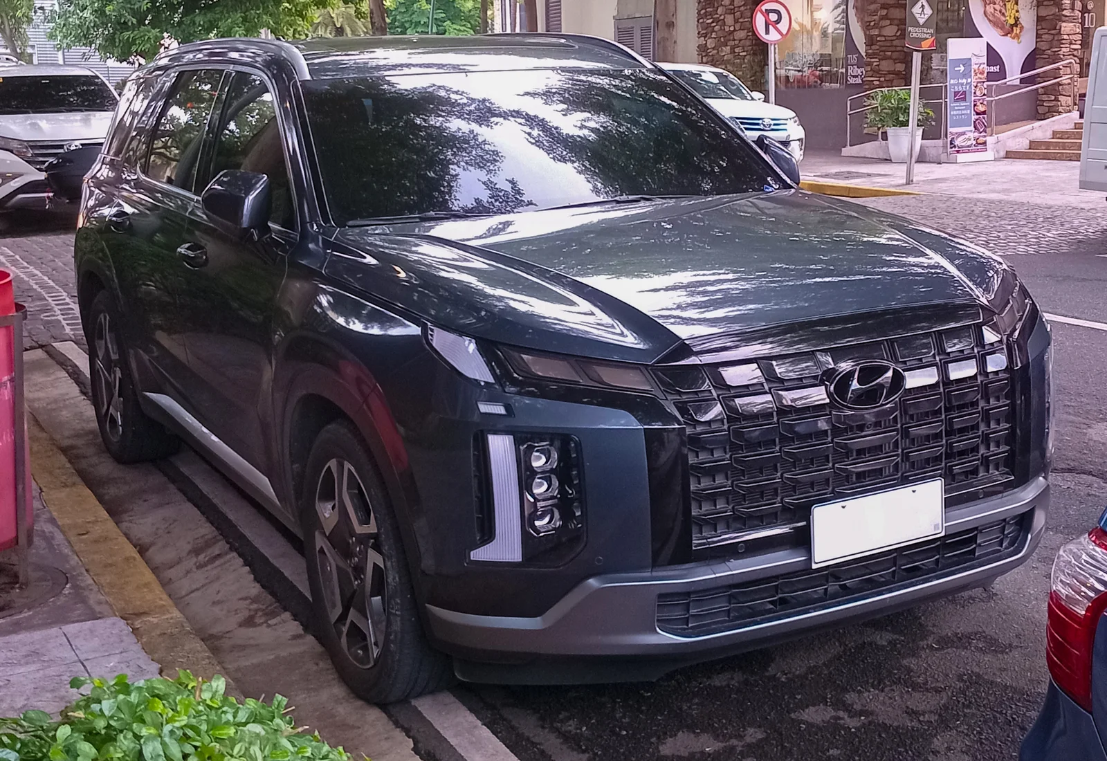 Dark-grey Hyundai Palisade, current facelift generation, front three-quarter view on a city street.