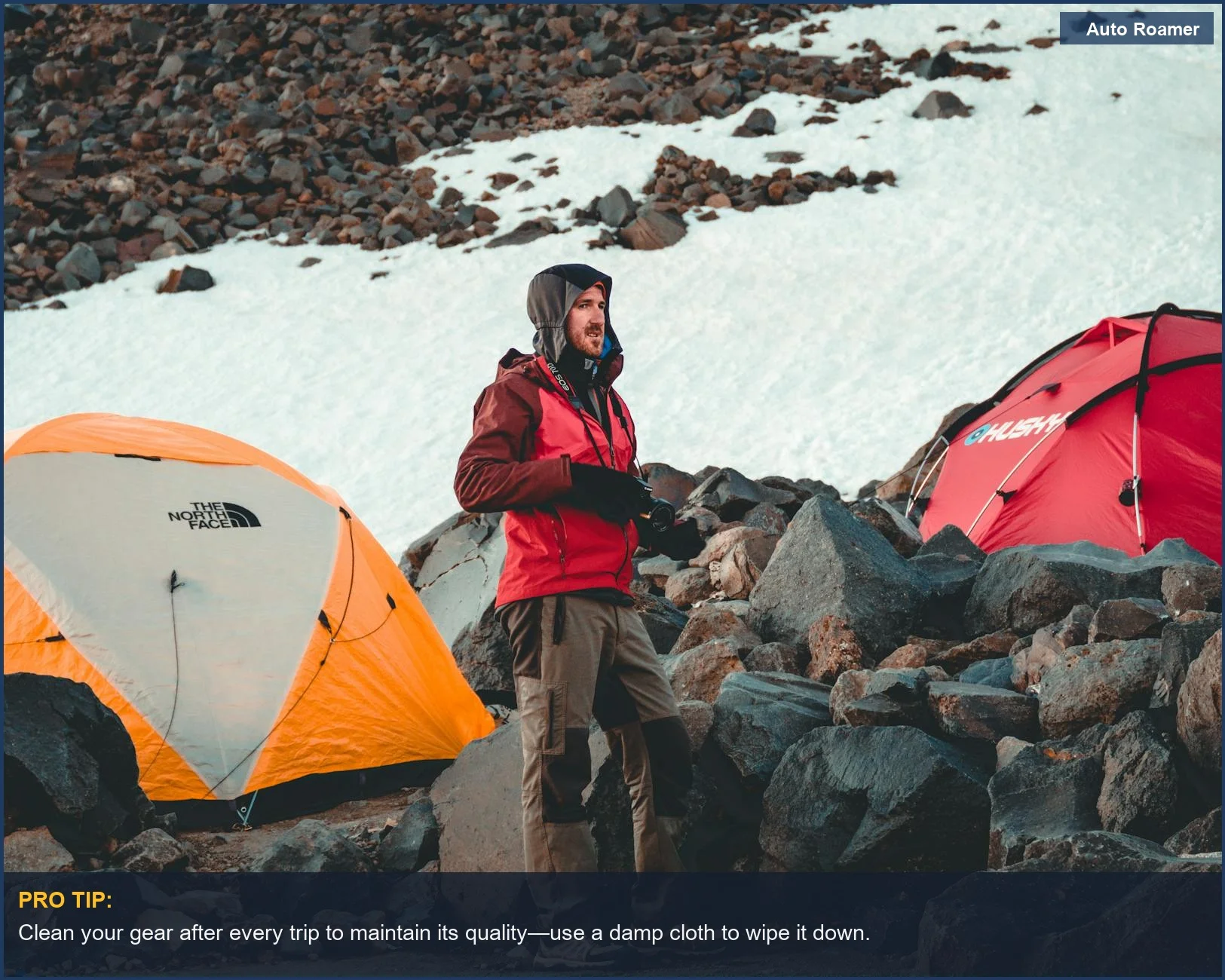 Man camping in a snow-covered mountain area, with tents set against rocky terrain, showcasing Kia Sportage gear durability.