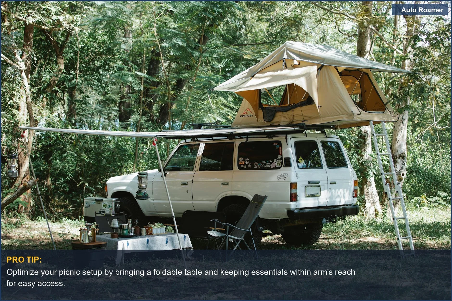 White Kia Sportage with rooftop tent set up for car camping in a green forest clearing with picnic supplies.