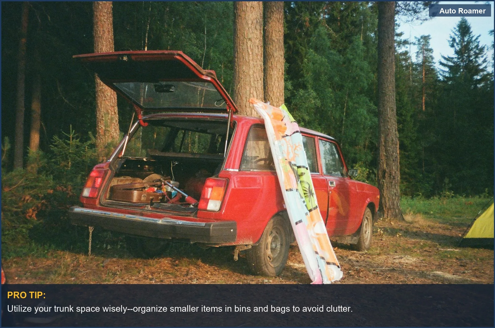Vintage red car trunk open, filled with camping gear in a forest clearing for car packing.