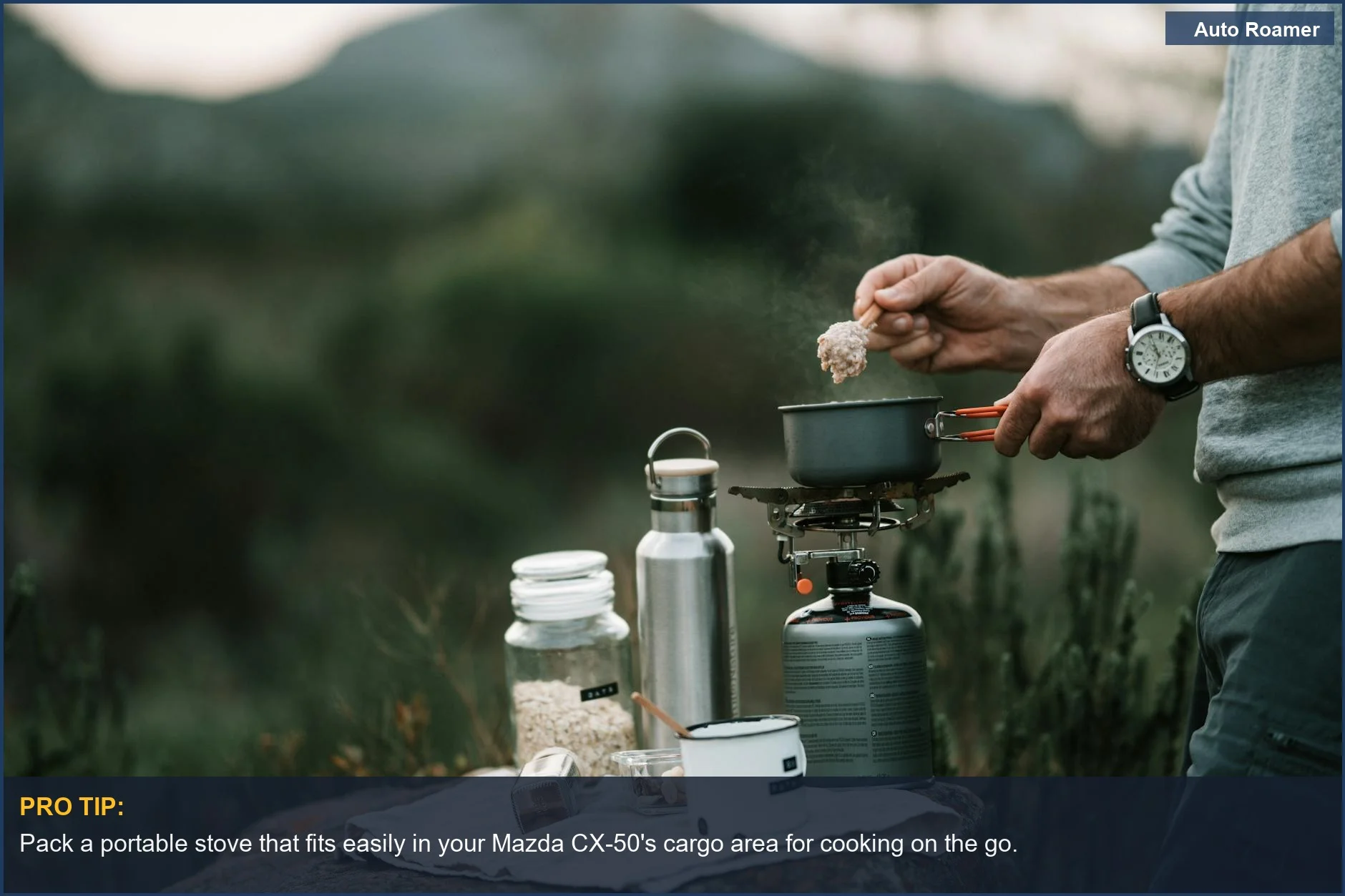 Person cooking on a portable stove at an outdoor campsite with a Mazda CX-50 nearby.