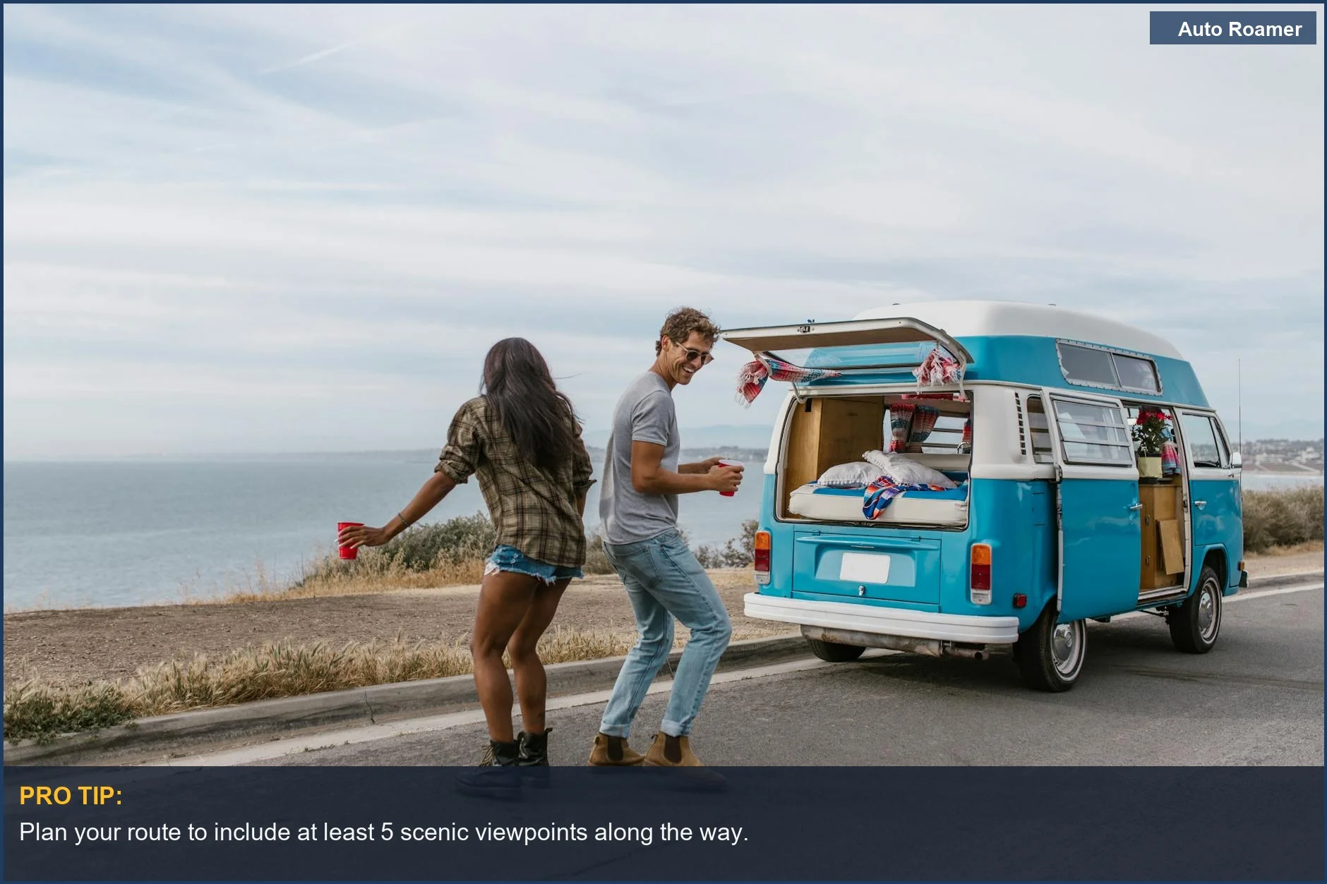 Happy couple dancing beside their blue campervan on a coastal road trip.