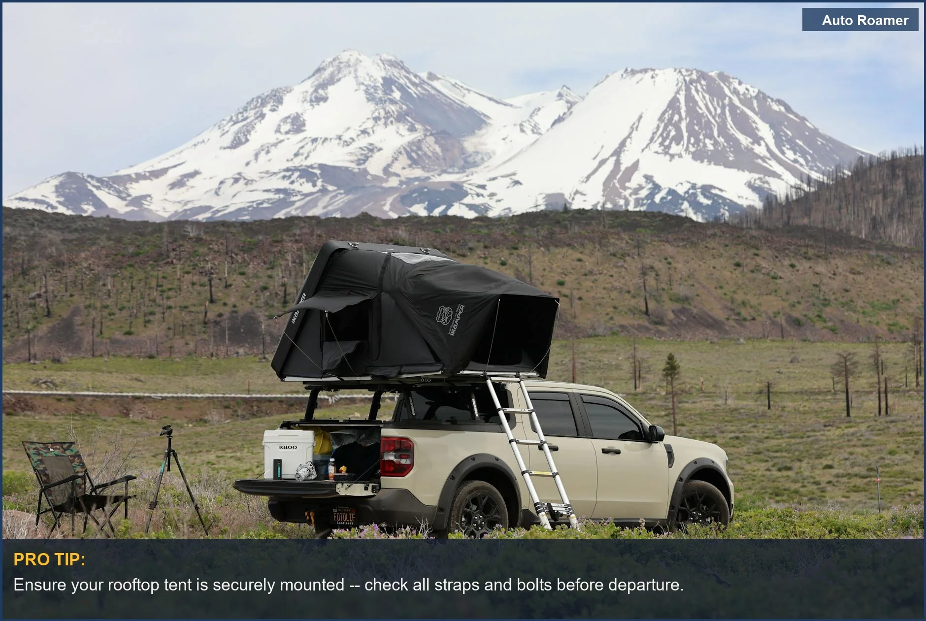 Pickup truck with rooftop tent set up in wilderness with snowy mountains in the background.