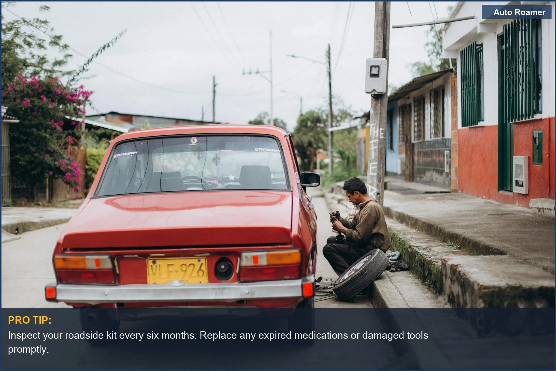 Mechanic performing manual roadside car repair on an urban street, highlighting the need for vehicle safety kit upkeep.