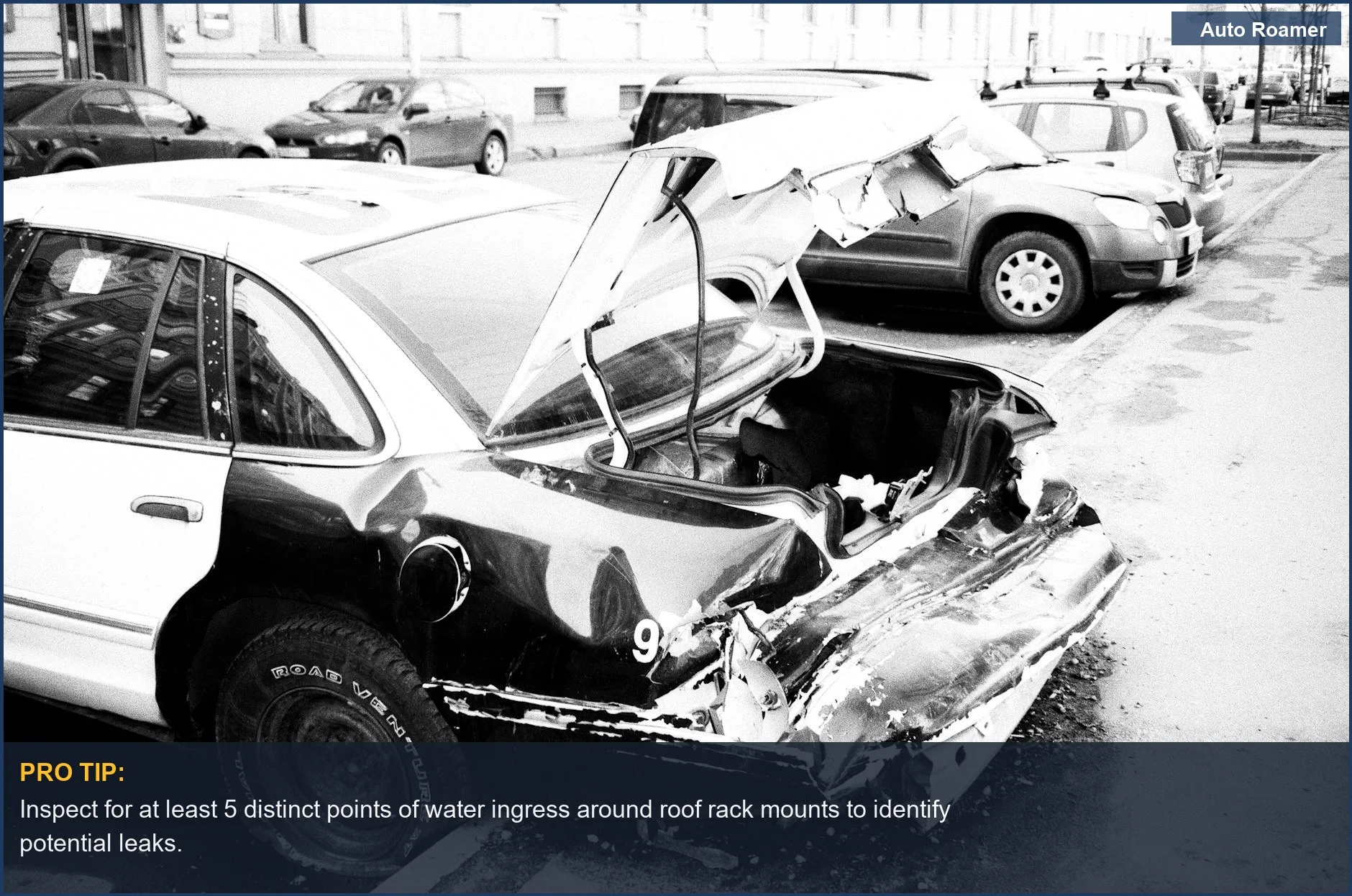 Urban street scene with a heavily damaged black and white car, illustrating severe roof rack installation damage.