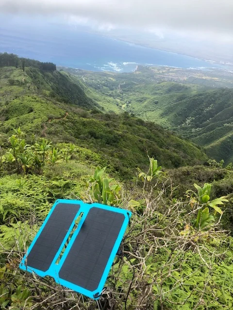 A compact portable solar charger set out on a hillside to catch the sun, the panel this fix checks for adequate voltage.