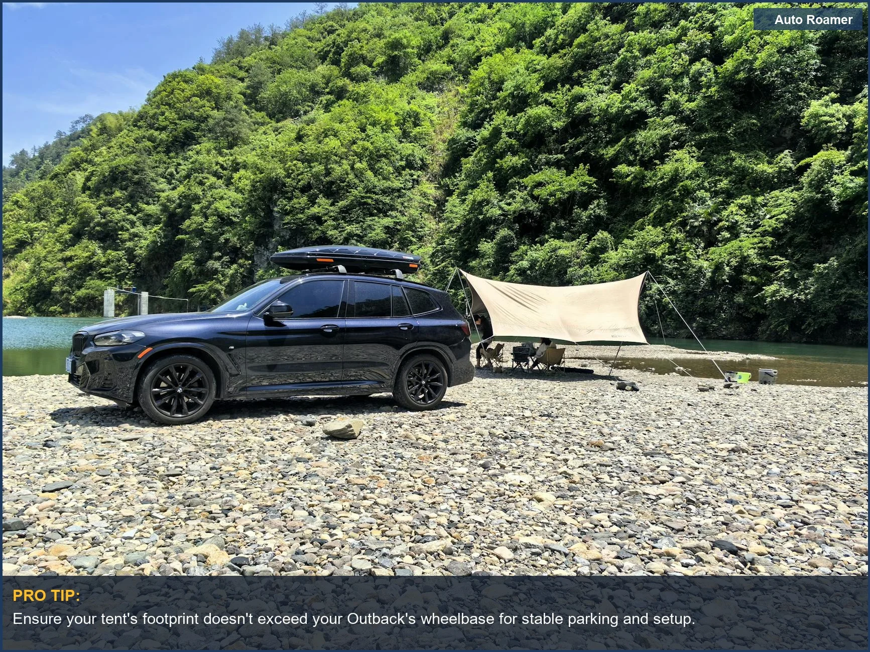 Black Subaru Outback parked by a river with a large tent and camping gear.