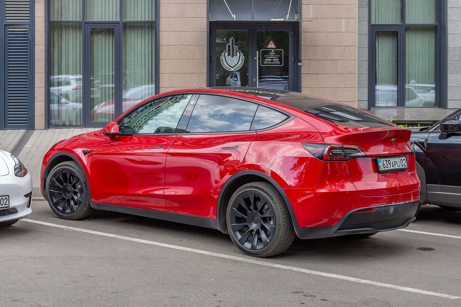 A white Tesla Model Y electric SUV parked on a city street in a side three-quarter view, compared here against rivals for camping.