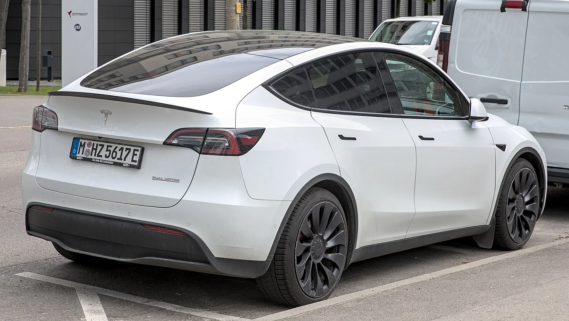 A white Tesla Model Y electric SUV seen from the rear three-quarter, the liftgate and cargo opening that matter when loading a camping setup to sleep in.