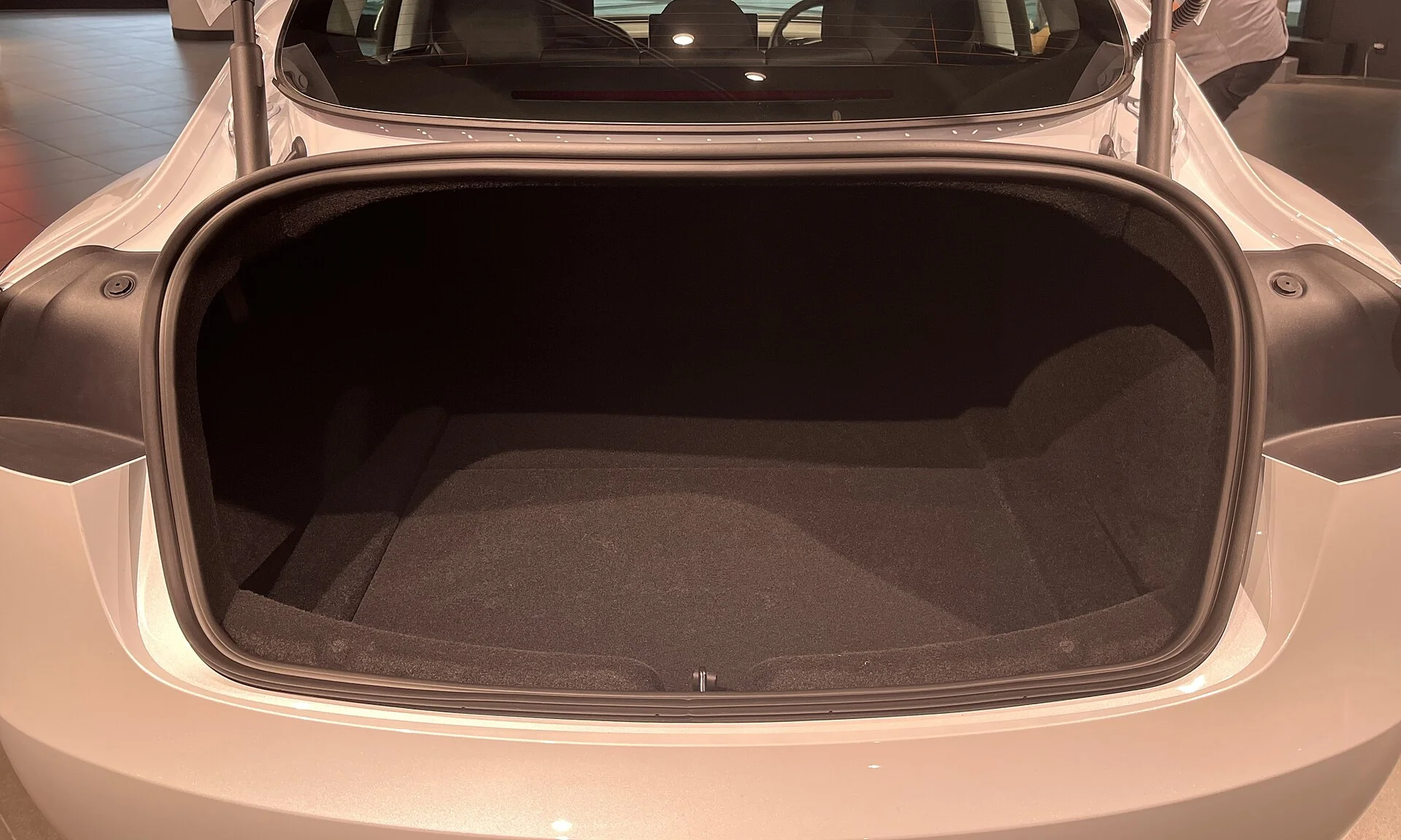 The open rear trunk of a white Tesla Model 3 sedan, showing the deep carpeted cargo well that this comparison weighs against the Model Y's flatter load bay.