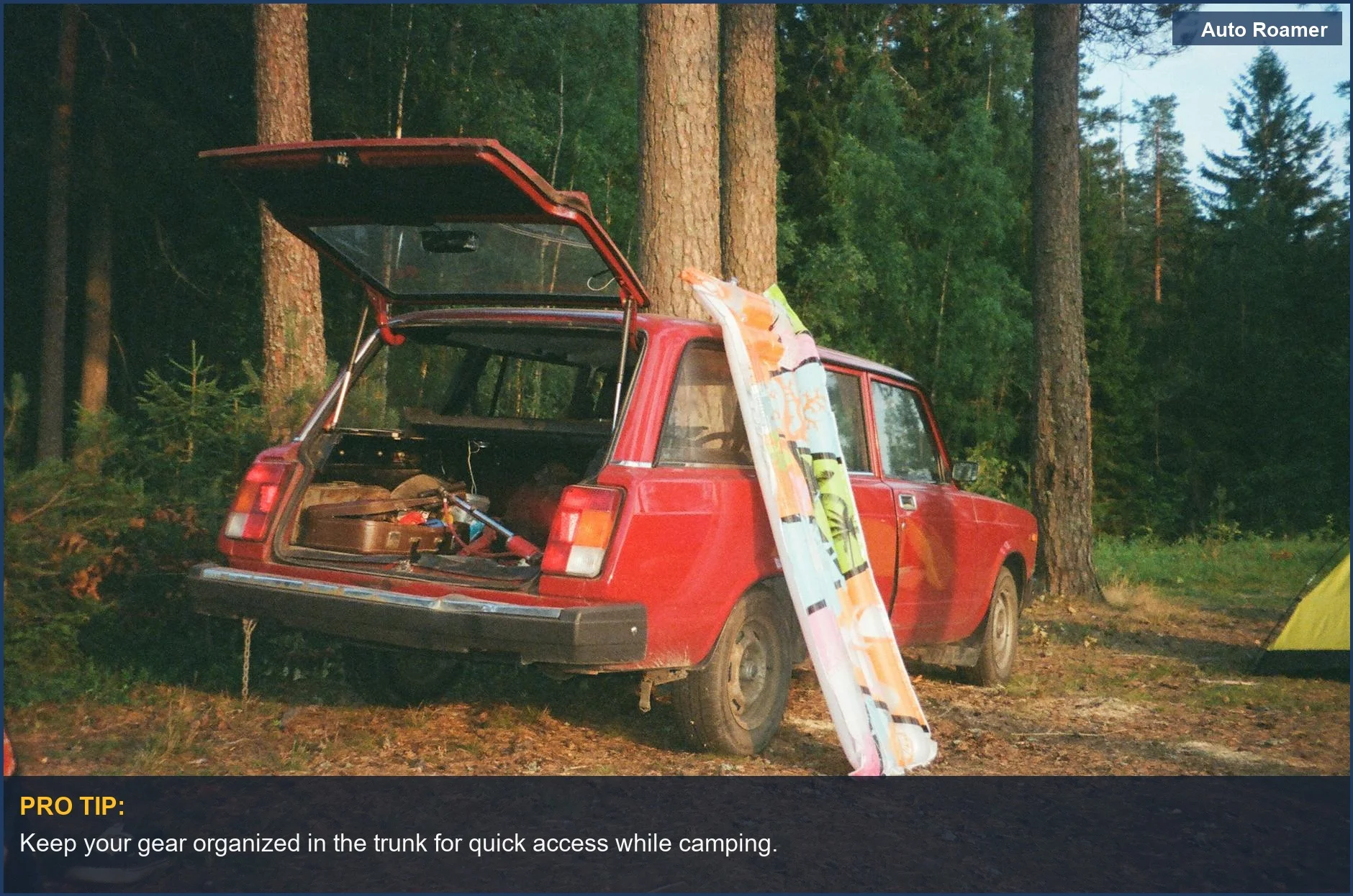 Vintage red car with open trunk displaying camping gear in a serene forest setting.