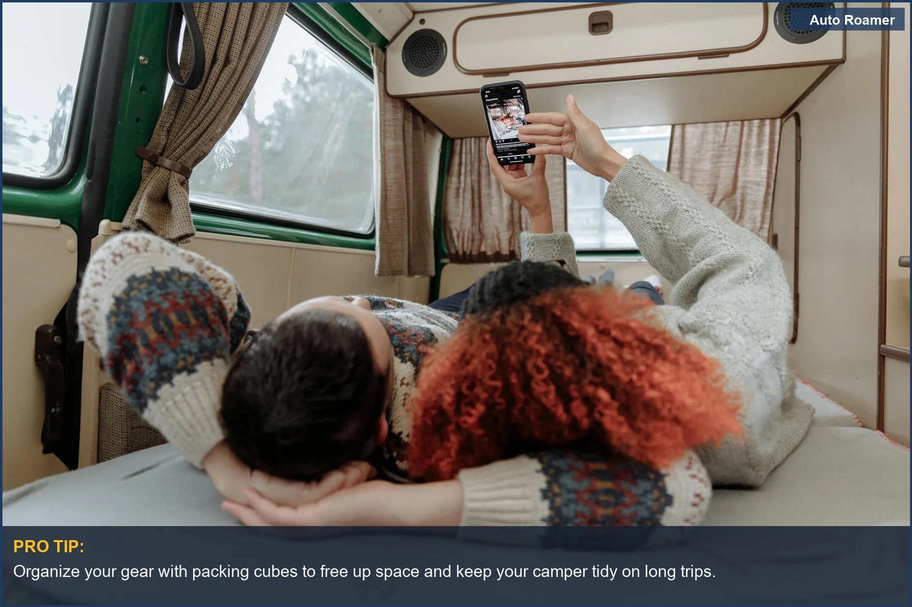 Couple lounging inside a cozy VW Transporter camper van, enjoying videos on their smartphone.
