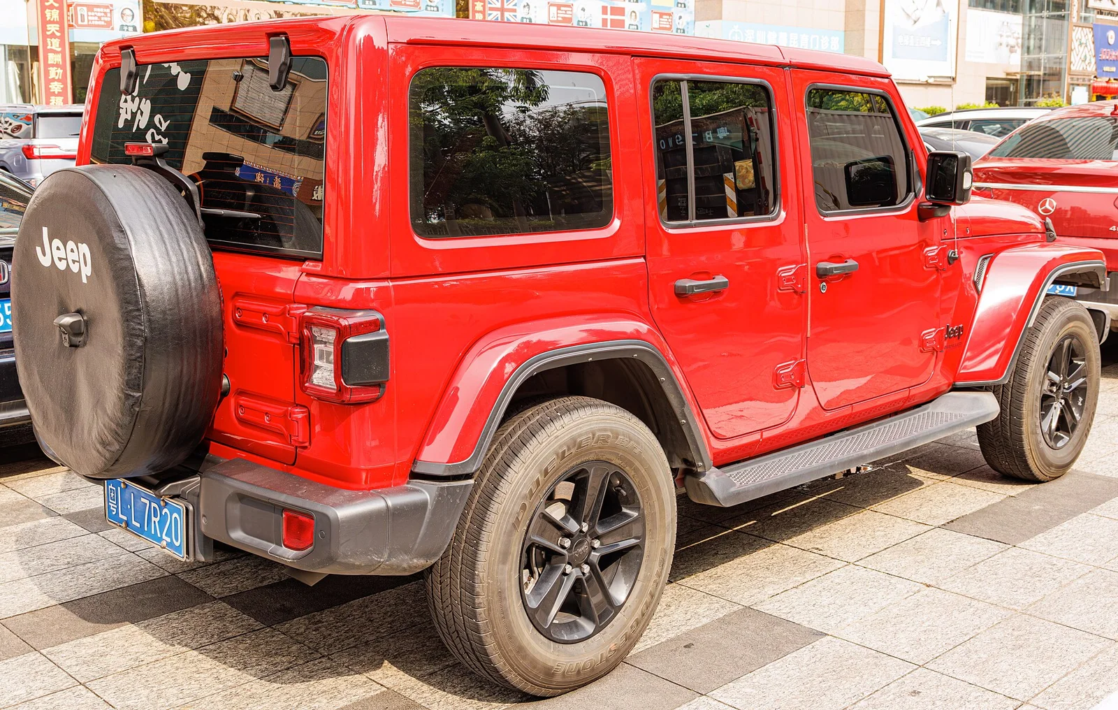 Red Jeep Wrangler Unlimited, current JL generation, four-door hardtop, rear three-quarter view with the spare wheel on the tailgate.