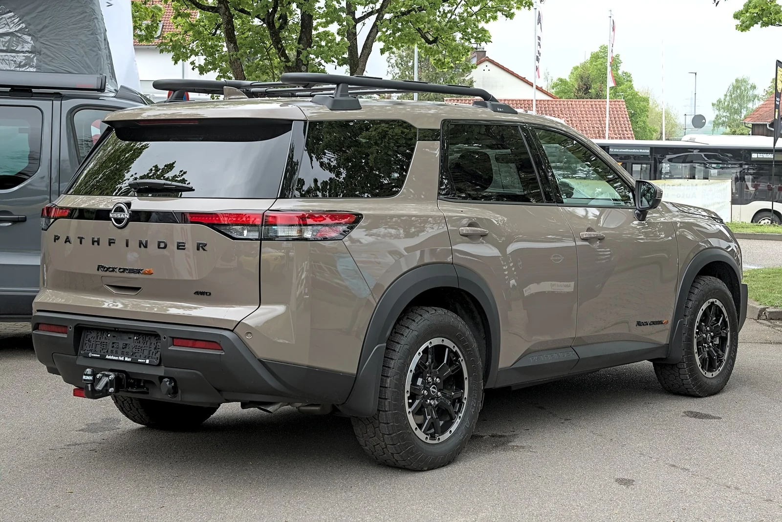 Tan Nissan Pathfinder Rock Creek, current R53 generation, rear three-quarter view showing the roof rack and tailgate.