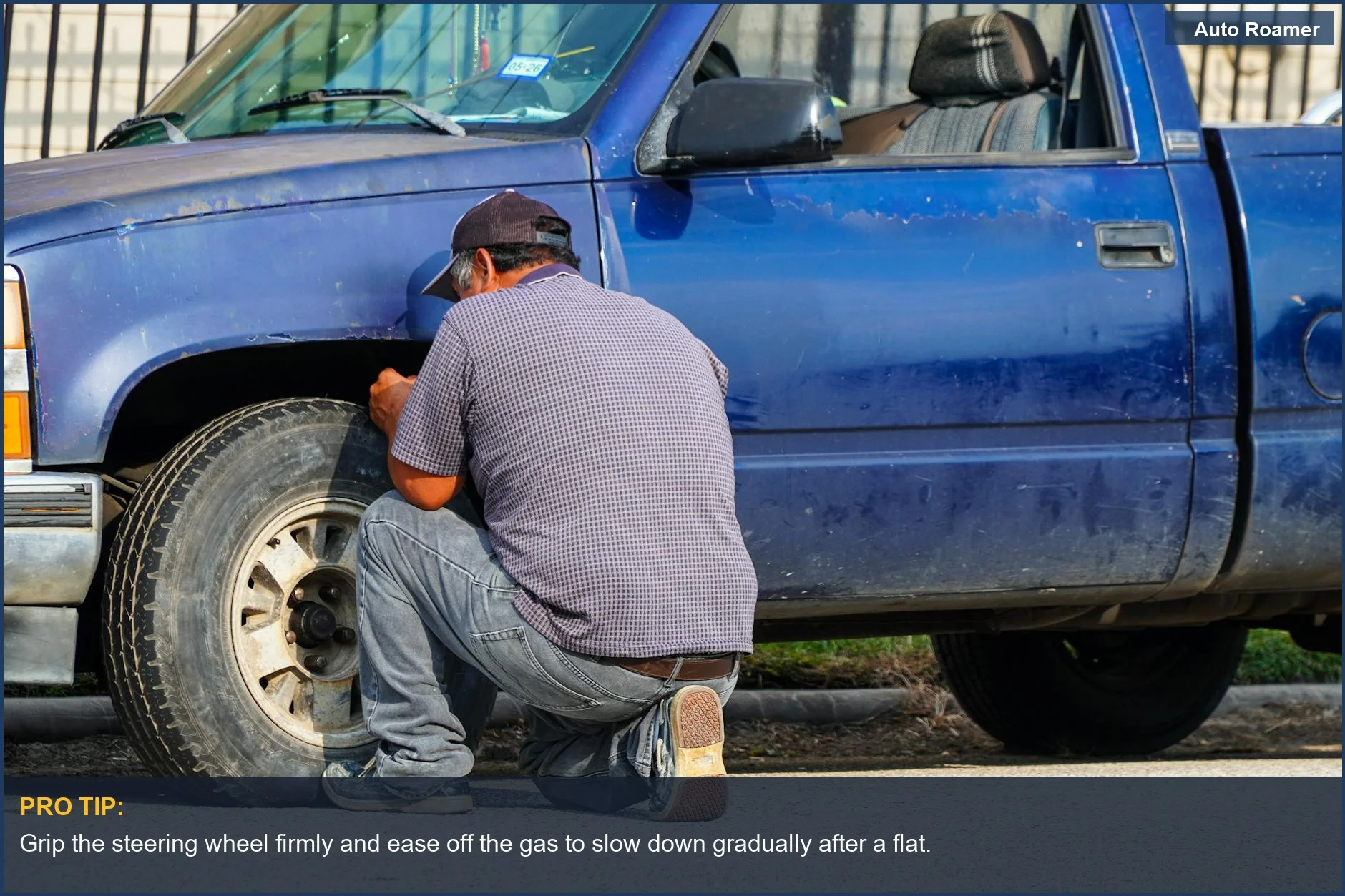 Man changing flat tire on a blue truck on a sunny remote road, emphasizing remote road safety.