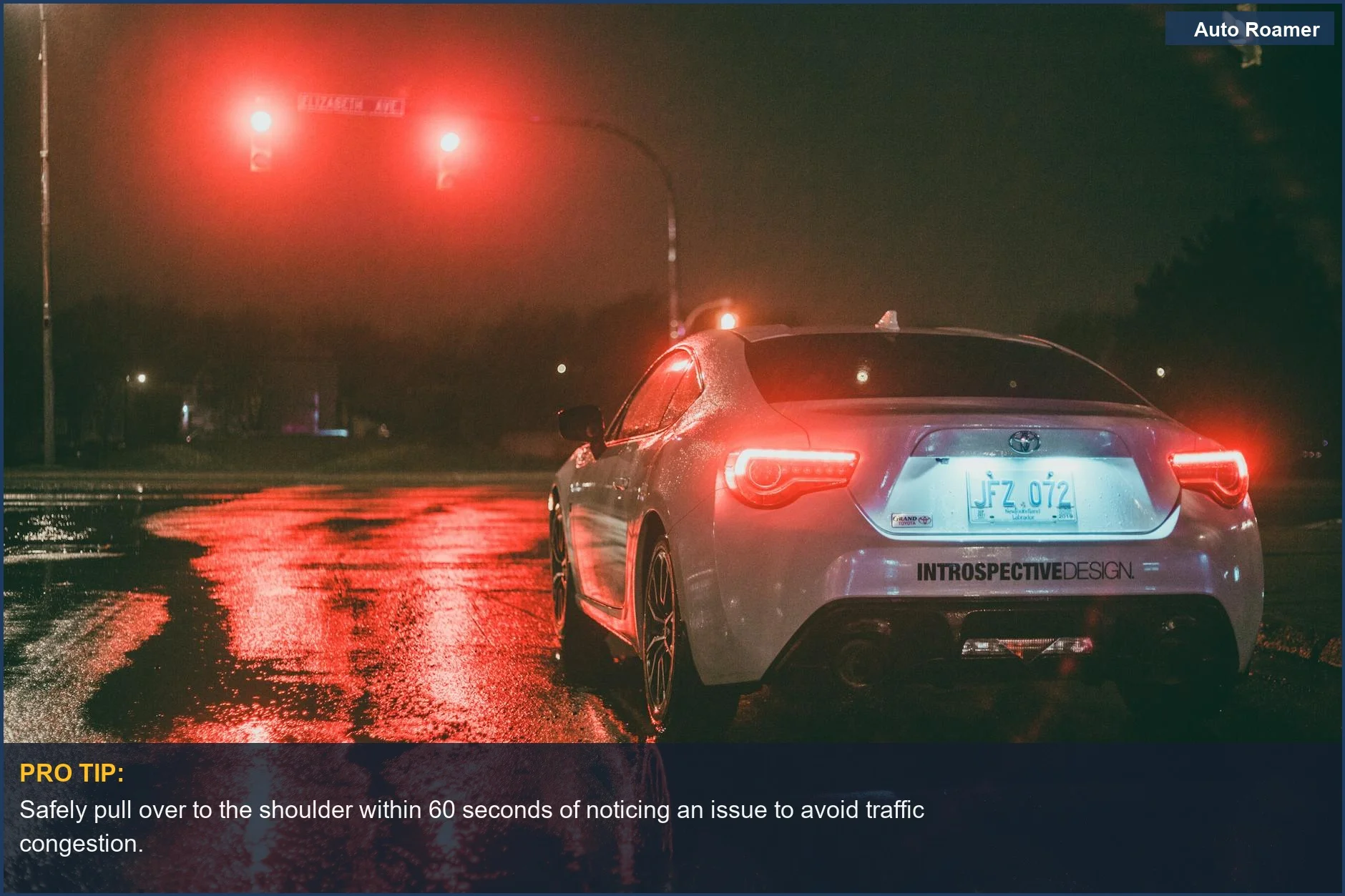 White car stopped at a wet urban intersection under red traffic lights at night, signaling a roadside emergency.