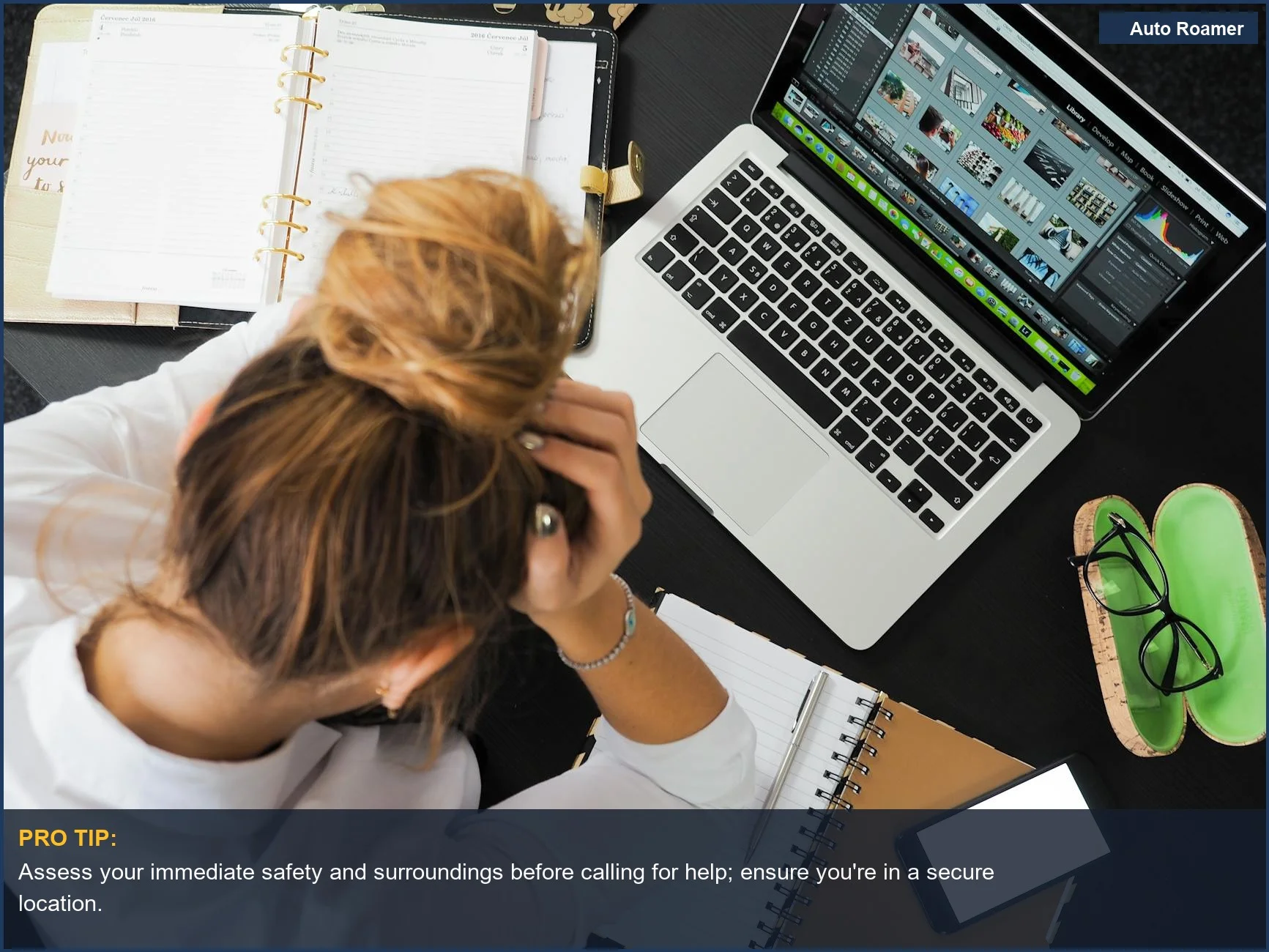 Overhead view of a stressed woman at a cluttered desk with a laptop, phone, and notebooks.