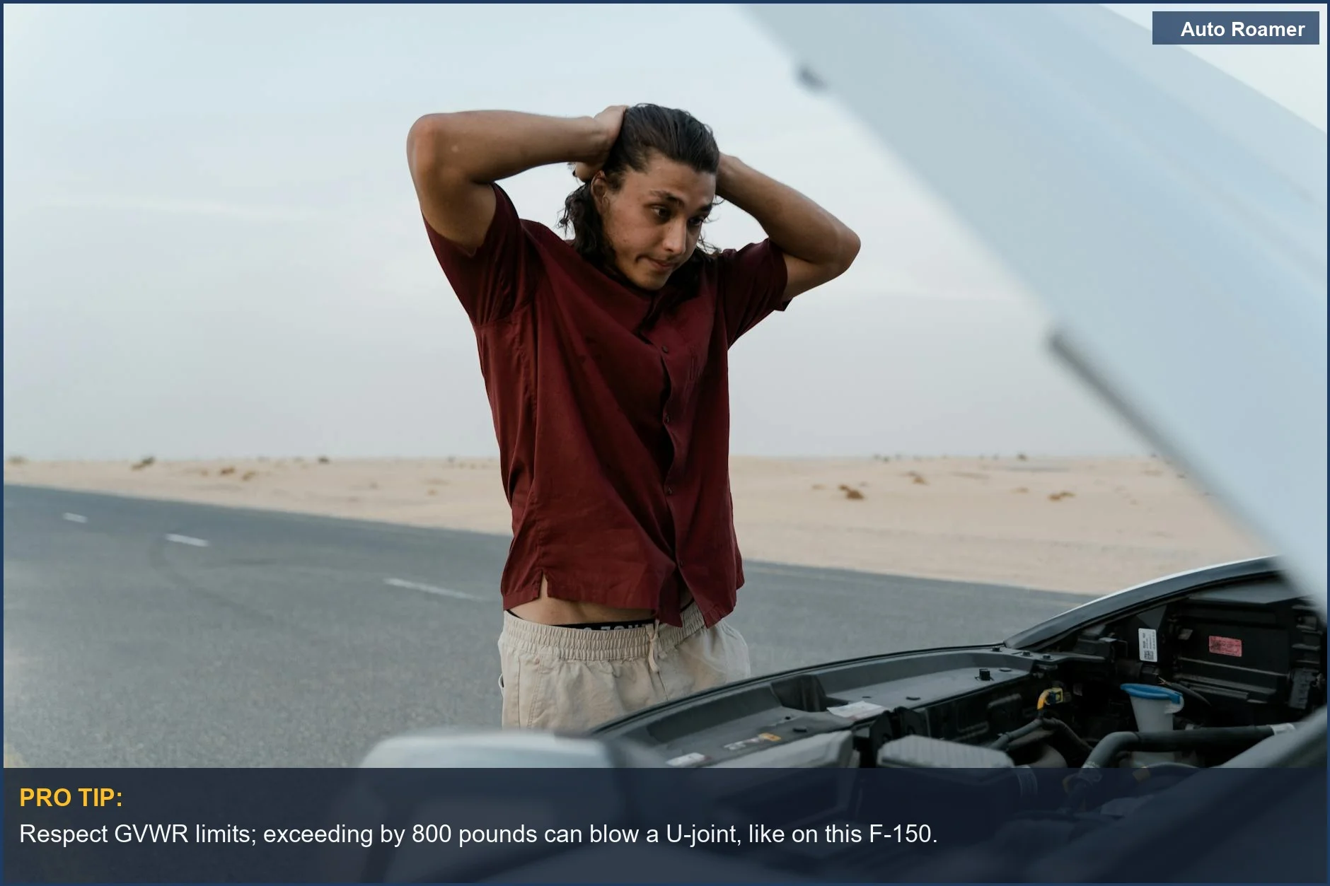 Stressed man inspects engine of broken car on deserted road, overloaded gear.
