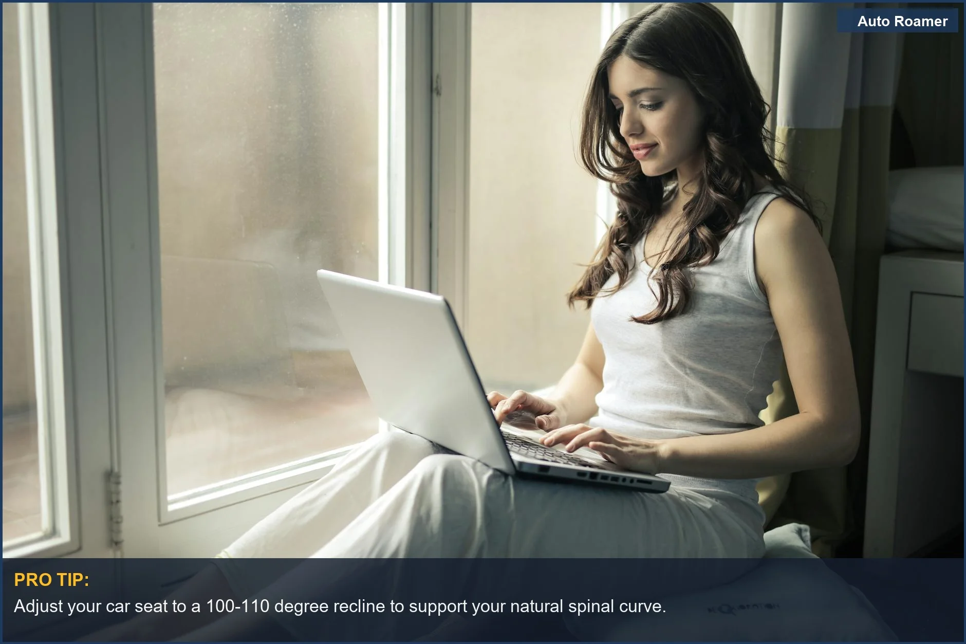 Woman working remotely on laptop by a window, highlighting poor posture and its impact on back pain from long drives.