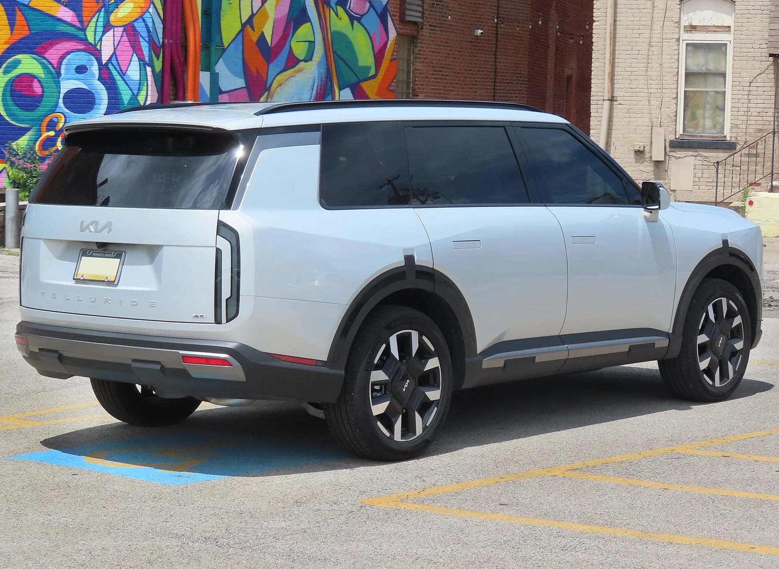 Silver Kia Telluride, rear three-quarter view showing the tailgate and roof rails where a cargo box mounts.