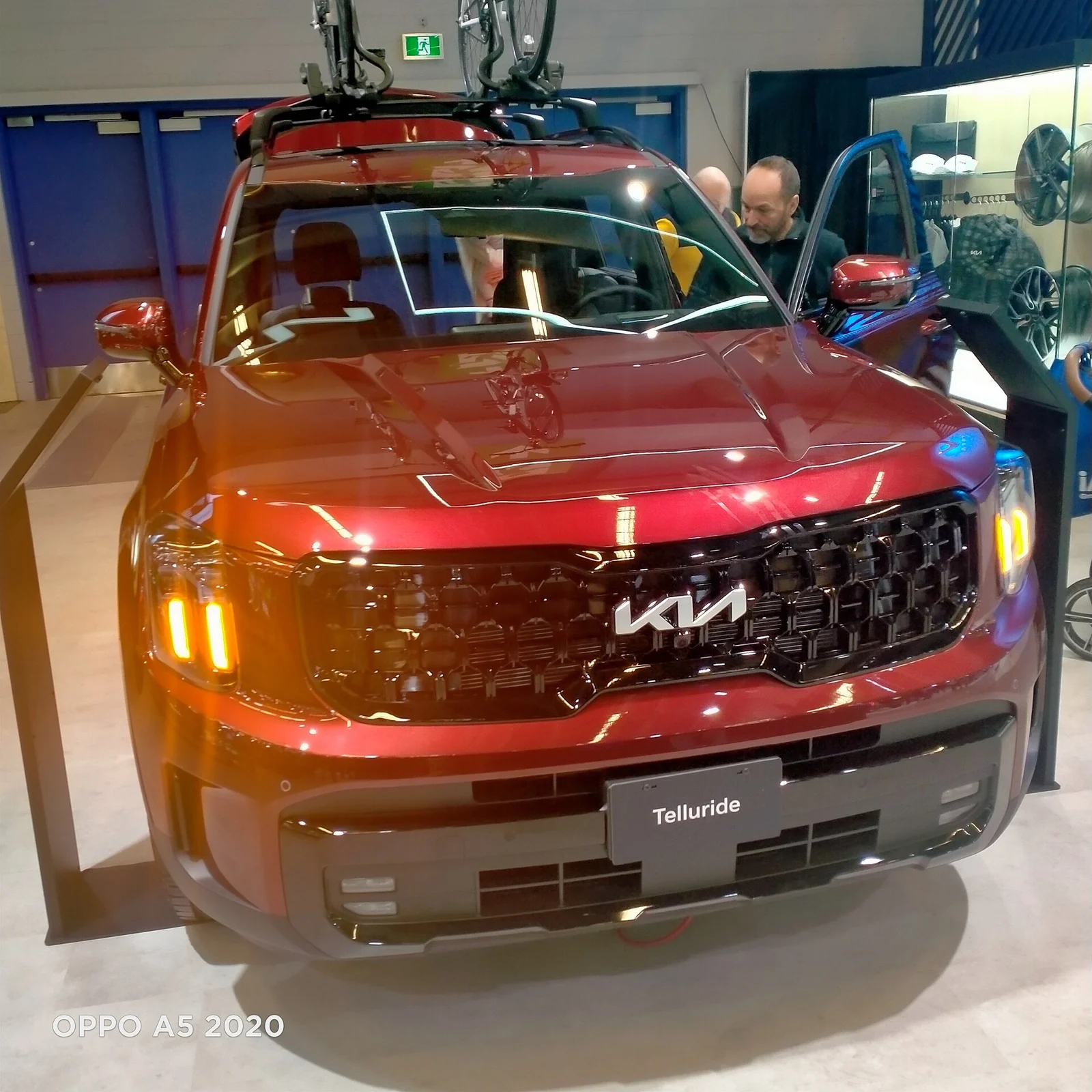 Red Kia Telluride, facelift generation, front three-quarter view with gear mounted on a roof rack.