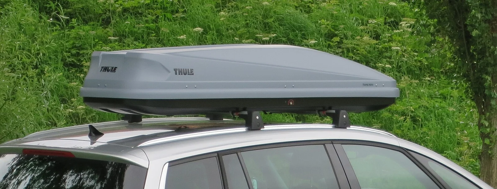 A silver rooftop cargo box mounted on a car's crossbars, the everyday setup this Yakima-versus-Thule guide walks through.